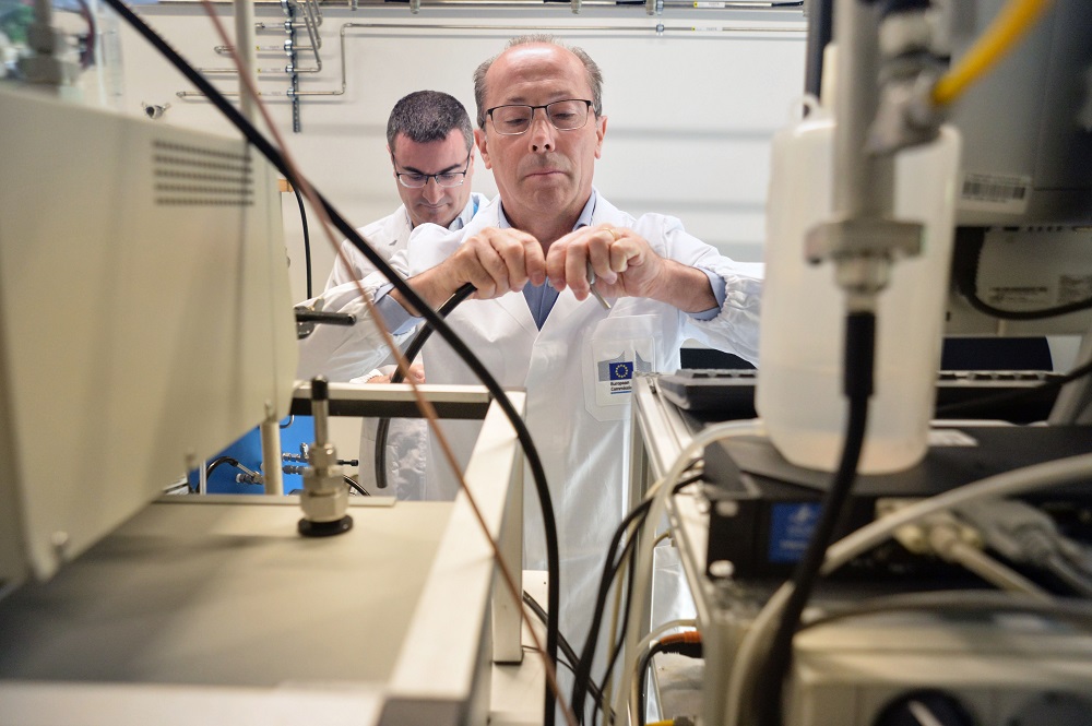 Naukowiec w białym fartuchu łączy w rękach dwa kable aparatury